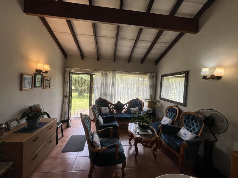 A cozy living room featuring exposed timber ceiling beams, terracotta floor tiles, and direct access to the garden through a glass-paneled door.