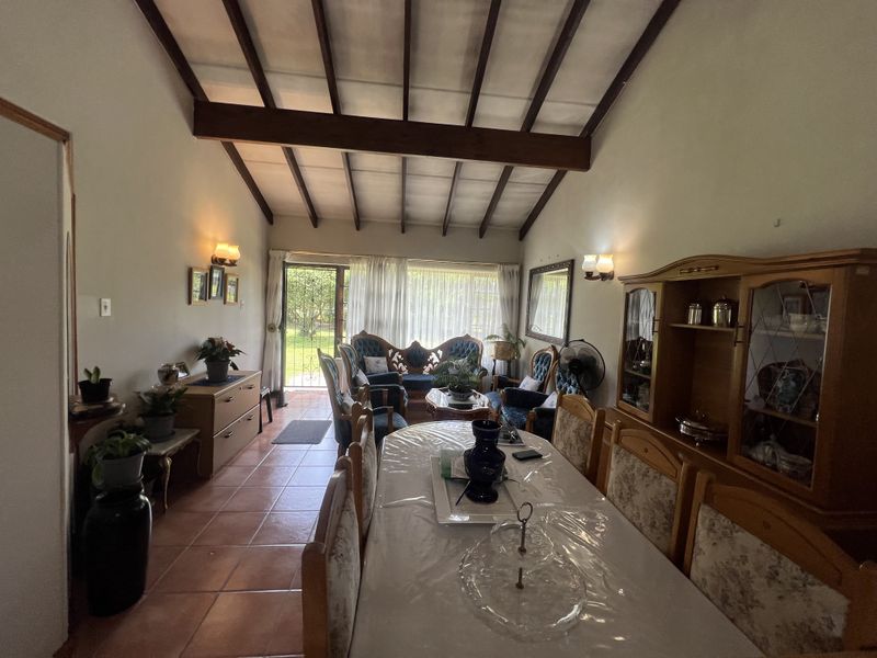 Spacious open-plan living and dining area featuring high vaulted ceilings with exposed timber beams and terracotta floor tiles.