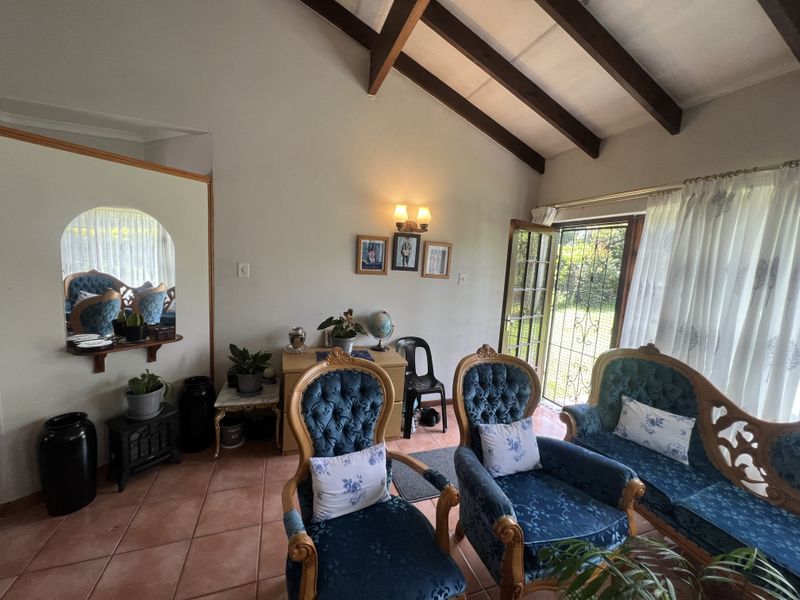 A living room featuring vaulted ceilings with exposed timber beams, terracotta floor tiles, and a glass-paneled door providing access to the garden.
