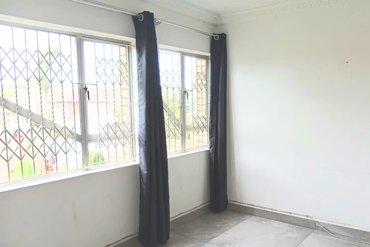 A bright, empty bedroom featuring large windows with security bars, tiled flooring, and decorative ceiling cornicing.
