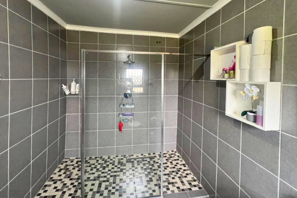 A modern walk-in shower featuring grey wall tiles, a mosaic-tiled floor, a glass enclosure, and a fixed shower head.