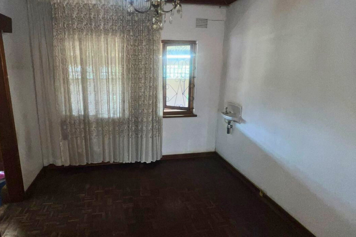 A dated interior room featuring dark parquet flooring, a small wall-mounted basin, and a timber-paneled ceiling.