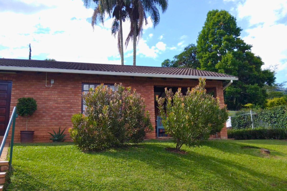 A view of the townhouse exterior featuring red brick facade, tiled roof, and a covered patio area set within a landscaped garden.