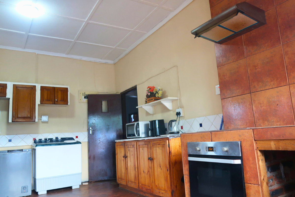 A dated kitchen featuring wooden cabinetry, a built-in oven with extractor fan, and tiled splashbacks, offering potential for modernization.
