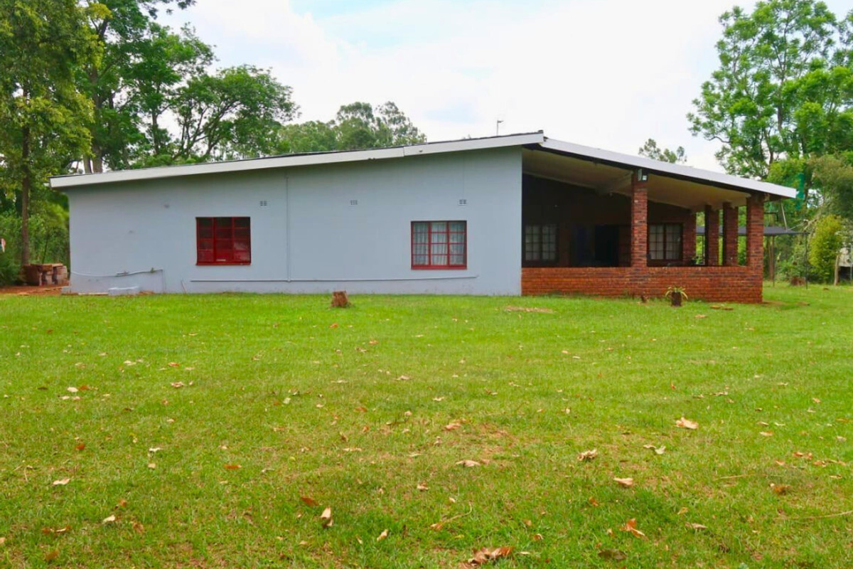 A side view of a single-story house featuring a painted exterior, brick patio pillars, and a large surrounding lawn.
