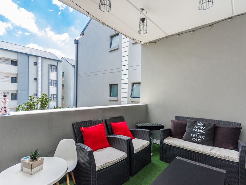 A covered balcony featuring a solid balustrade, pendant lighting, and artificial turf flooring, offering a private outdoor space.