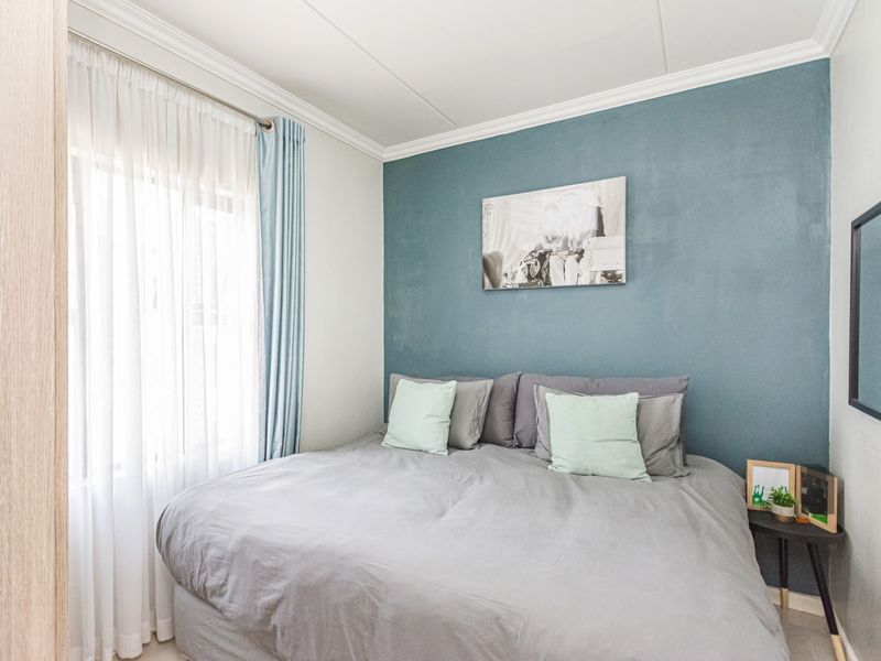 A well-maintained bedroom featuring a blue accent wall, crown molding, and natural light through a window.