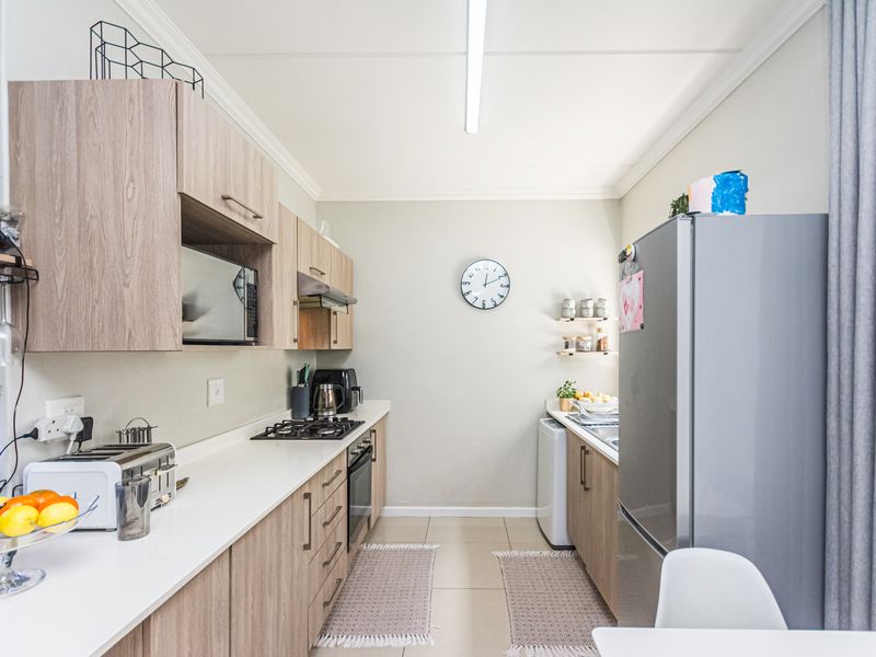 A well-maintained galley-style kitchen featuring light wood-grain cabinetry, a gas hob, built-in oven, and modern tiled flooring.