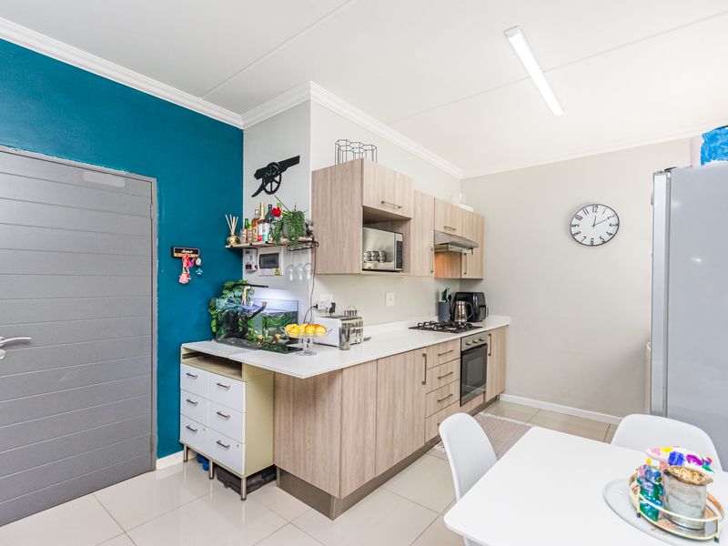 A functional kitchen featuring light wood-finish cabinetry, built-in oven and hob, extractor fan, and tiled flooring, complemented by a bold teal accent wall.