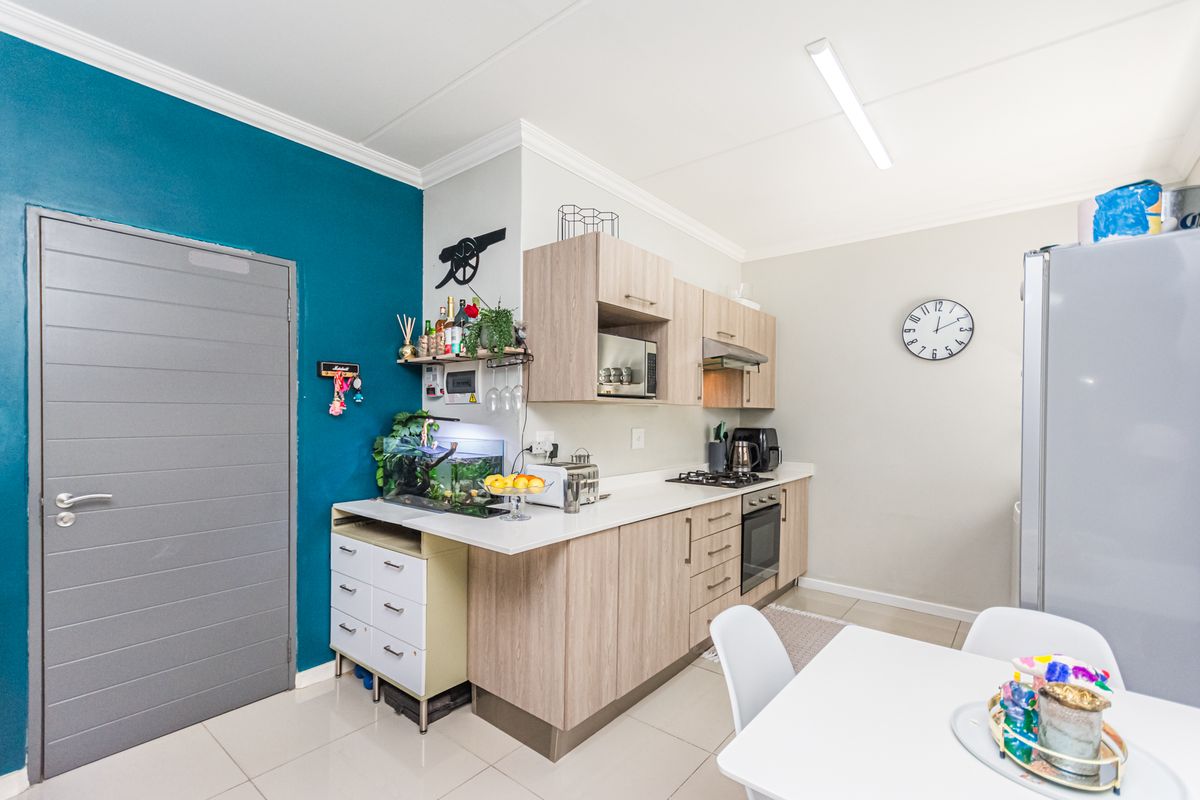 A functional kitchen featuring light wood-finish cabinetry, built-in oven and hob, extractor fan, and tiled flooring, complemented by a bold teal accent wall.