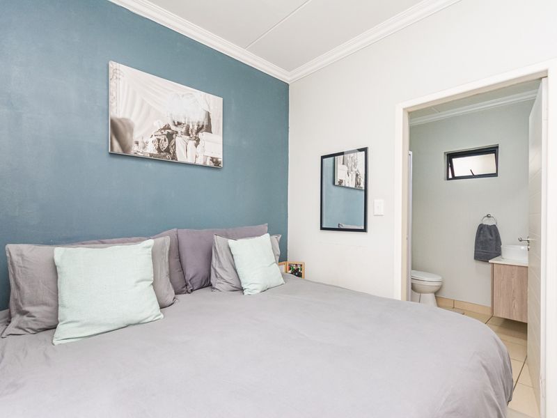 A well-maintained bedroom featuring a blue accent wall, crown molding, and an adjoining en-suite bathroom with a vanity and toilet.