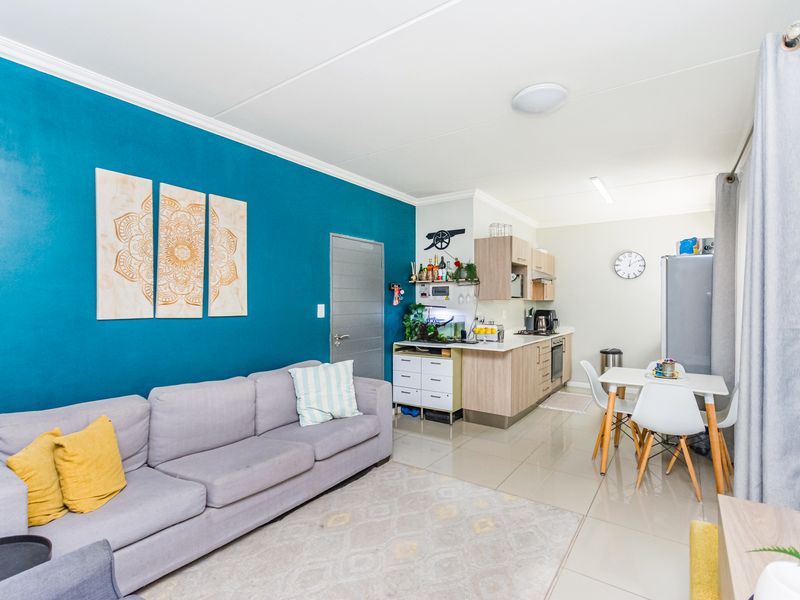 Open-plan living area featuring a modern kitchen with built-in cabinetry, hob, and oven, seamlessly flowing into a comfortable lounge space with tiled flooring.