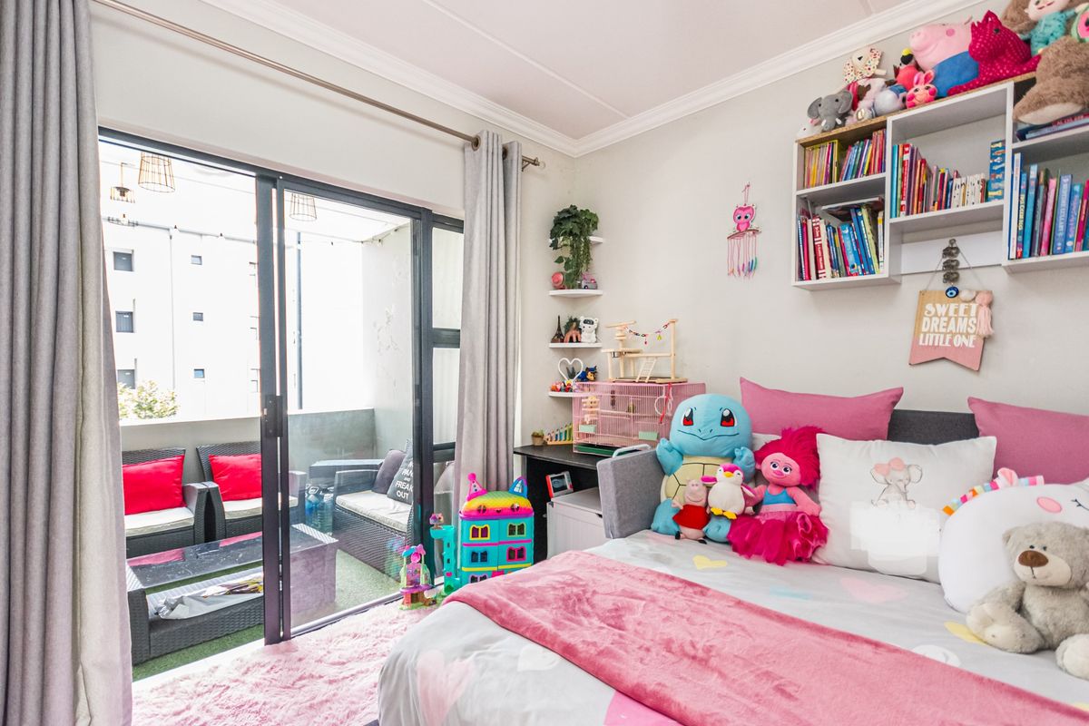 A bright bedroom featuring crown molding, built-in wall shelving, and a large sliding glass door providing direct access to a private balcony.