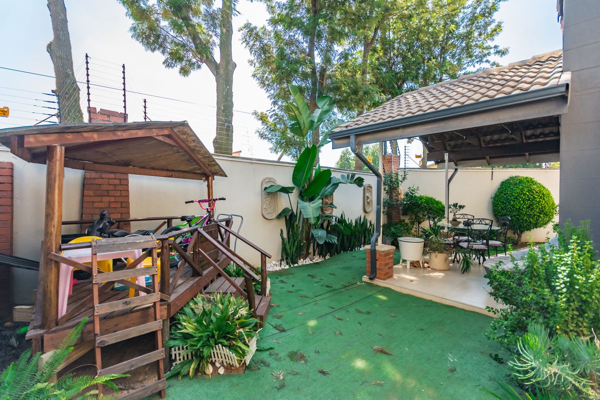 A private rear garden featuring a covered patio area, perimeter wall with electric fencing, and a raised wooden play structure.