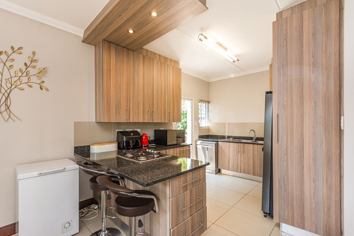 Modern kitchen featuring wood-finish cabinetry, granite countertops, a gas hob, and tiled flooring with ample storage space.