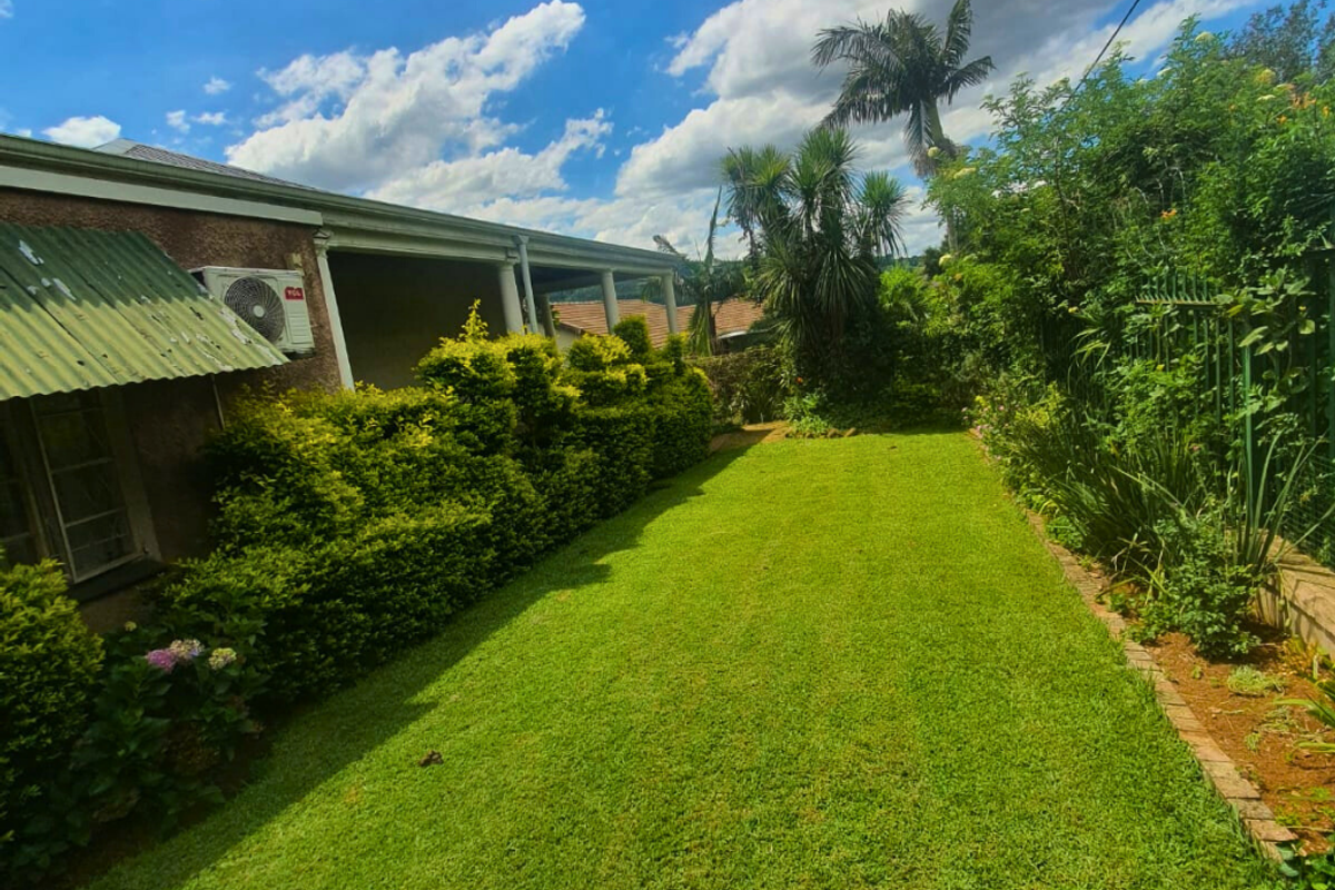 A well-maintained rear garden featuring a lush green lawn, established shrubbery, and a covered patio area attached to the main house structure.