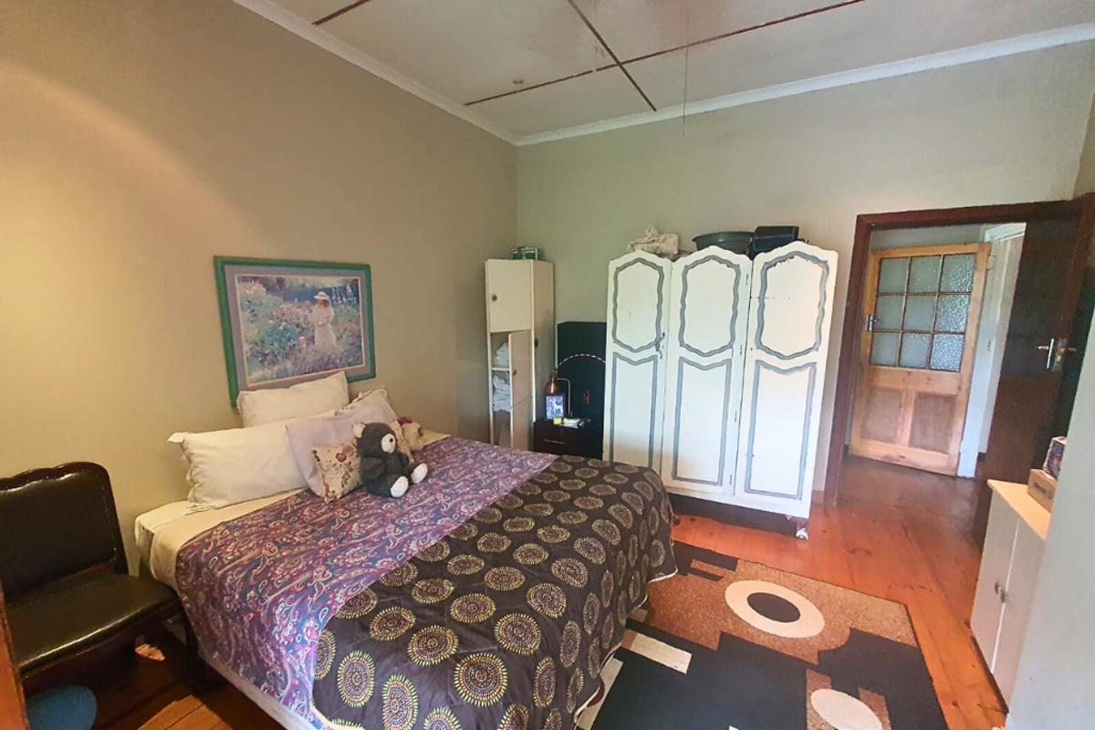 A bedroom featuring original timber flooring, a classic wooden door with glass panels, and a ceiling fan.