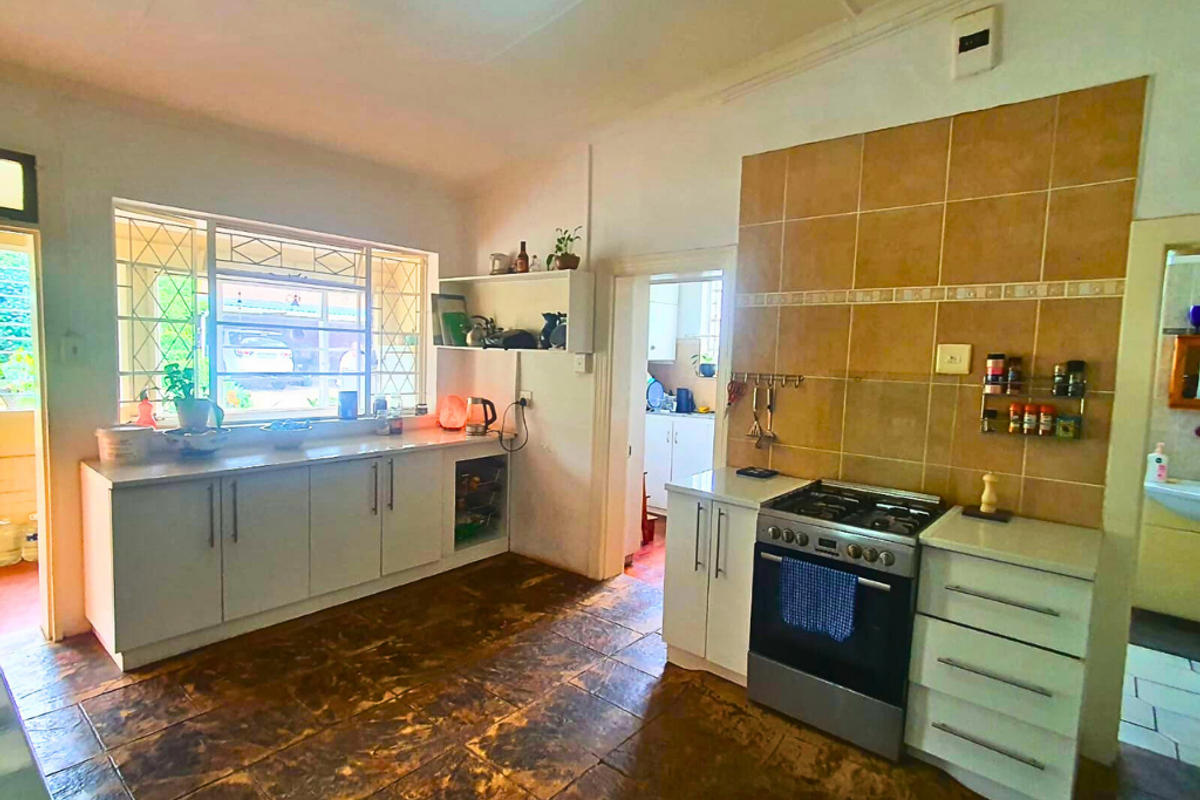 A functional kitchen featuring white cabinetry, a freestanding gas stove, and tiled flooring, with an adjacent scullery area visible through the doorway.