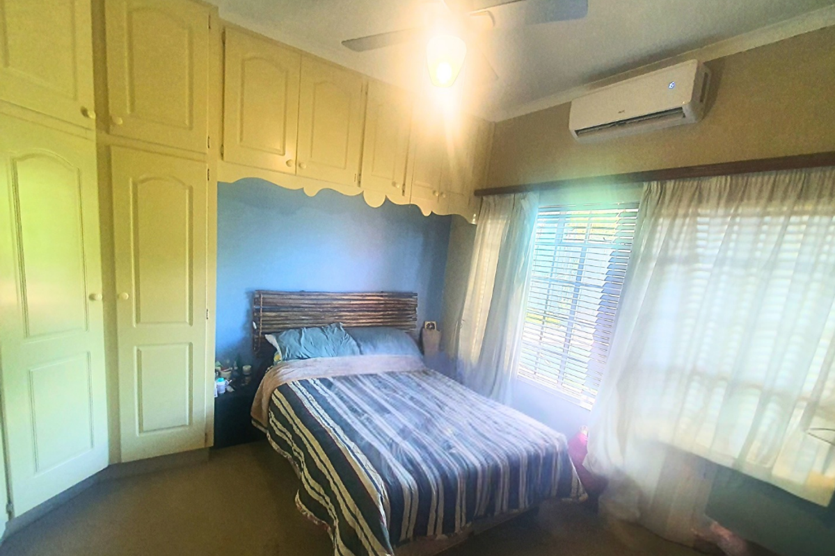 A bedroom featuring built-in floor-to-ceiling cabinetry, a ceiling fan, and a wall-mounted air conditioning unit.