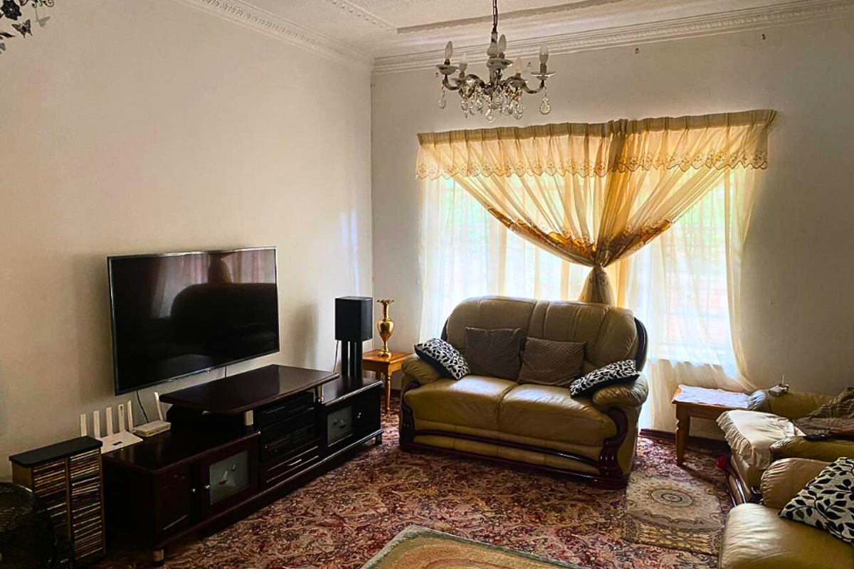 A traditional living room featuring ornate ceiling cornicing, a classic chandelier, and large windows with natural light.