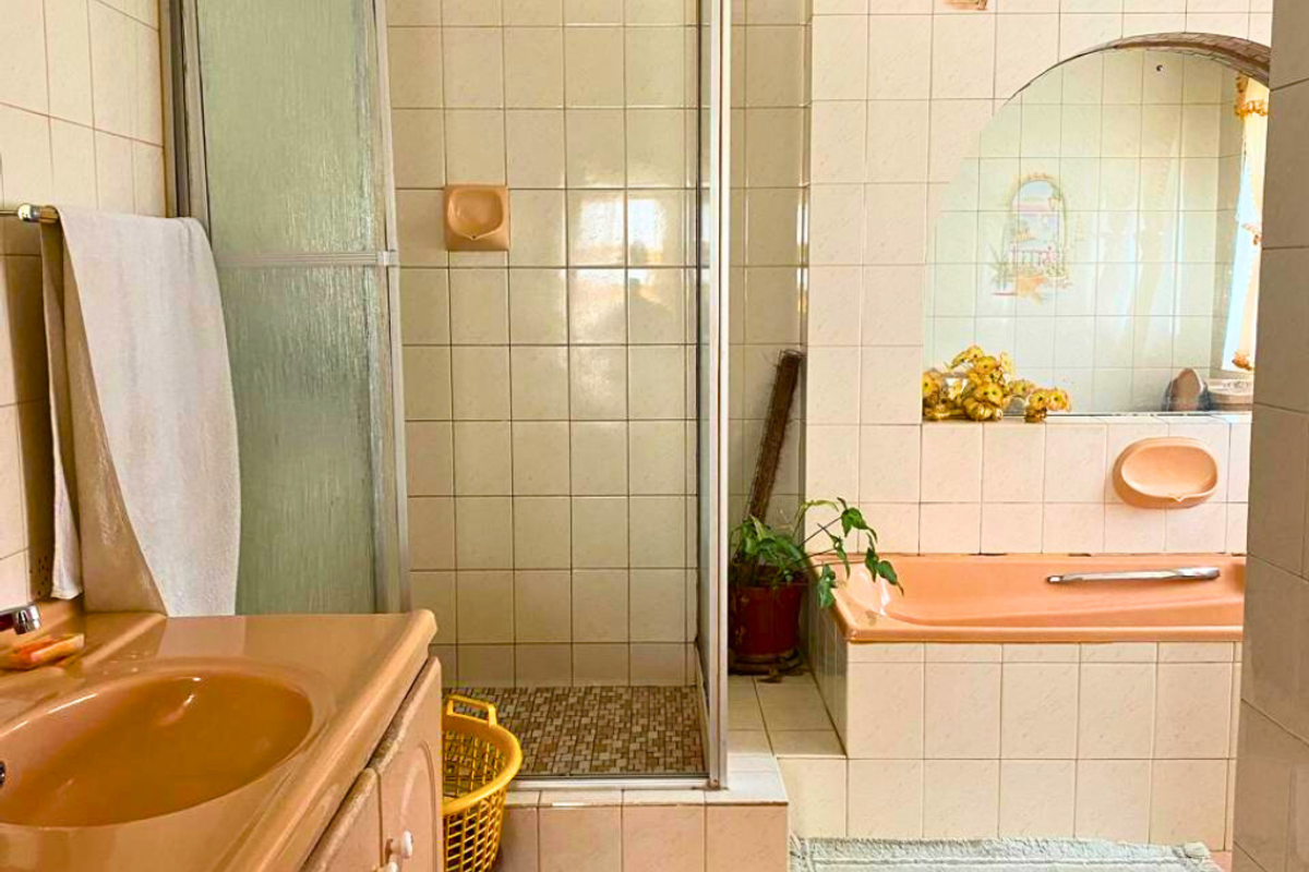 A dated bathroom featuring a built-in peach-toned bathtub, a separate glass-enclosed shower, and a matching vanity basin with tiled walls.