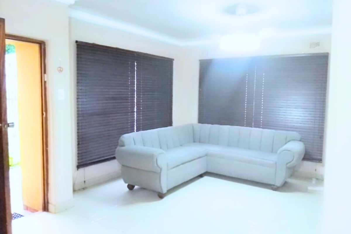 A bright living room featuring tiled flooring, neutral walls, and dark wooden blinds, providing a clean and functional space.