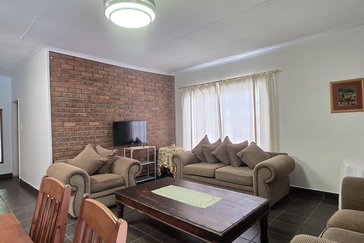 A living room featuring an exposed brick accent wall, tiled flooring, and coved ceiling finishes, providing a functional and comfortable living space.