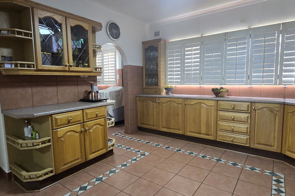 Spacious kitchen featuring traditional timber cabinetry, tiled flooring, and plantation shutters, offering a functional layout with ample storage and counter space.