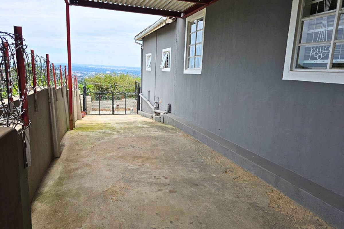 Side exterior area featuring a covered walkway, concrete paving, security fencing with razor wire, and views of the surrounding landscape.