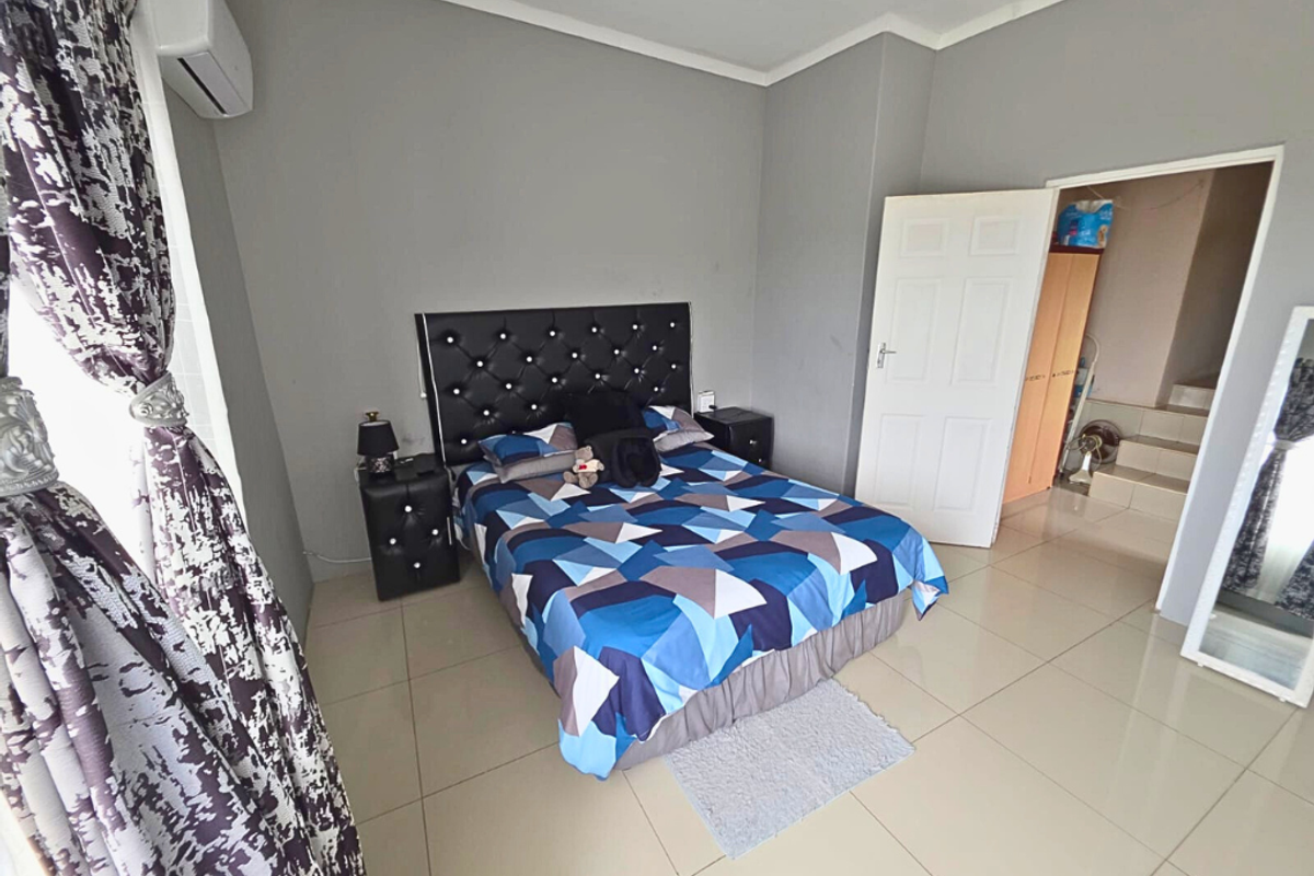 A bedroom featuring tiled flooring, a wall-mounted air conditioning unit, and a doorway leading to an adjacent space.