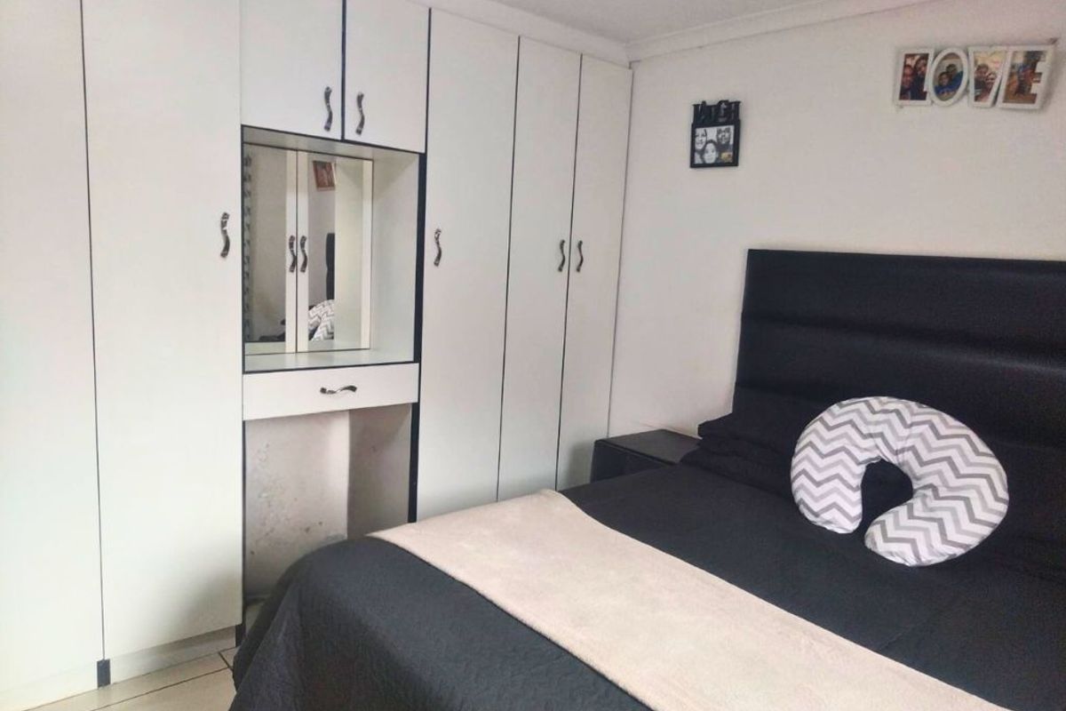 A bedroom featuring white built-in cupboards with an integrated vanity unit and tiled flooring.