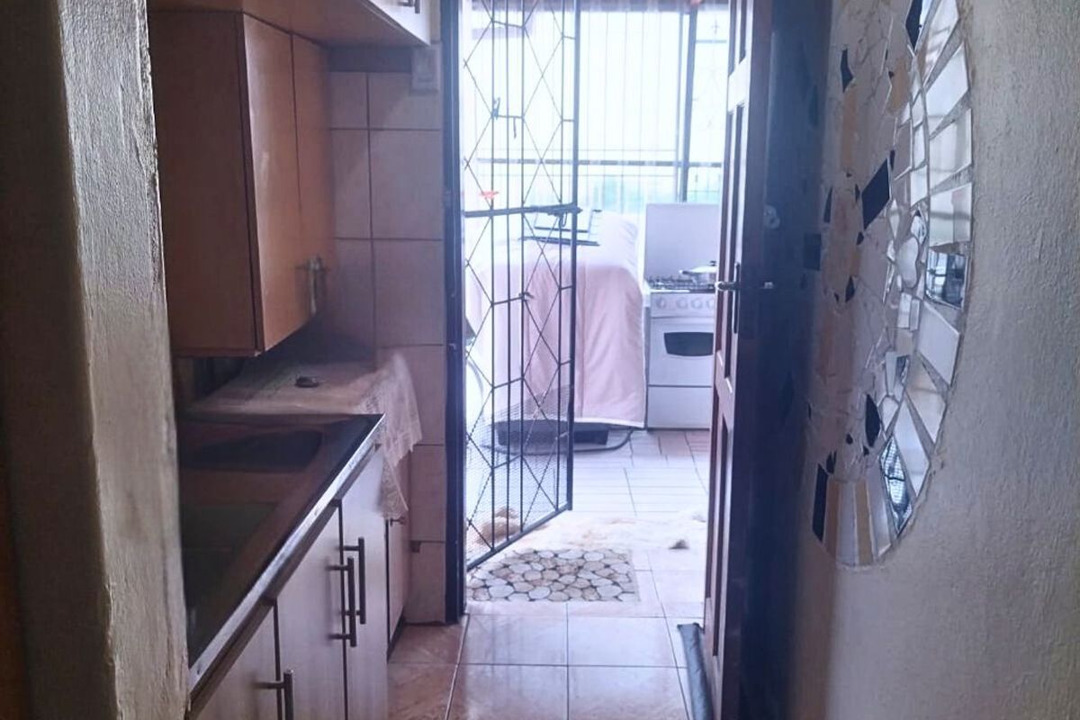 A narrow kitchen area featuring built-in wooden cabinetry and tiled flooring, leading directly out to a covered patio space.