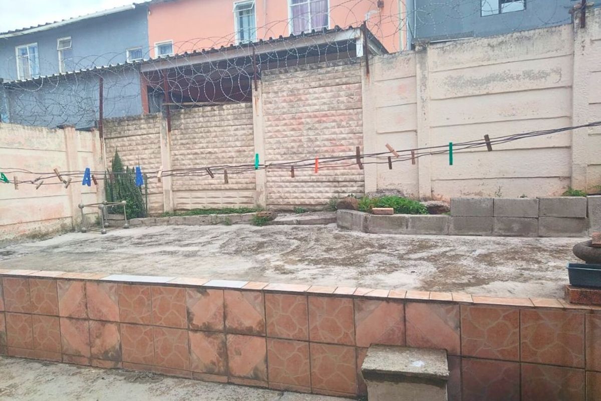 A rear courtyard area featuring concrete paving, a tiled retaining wall, and high perimeter walls topped with security razor wire.