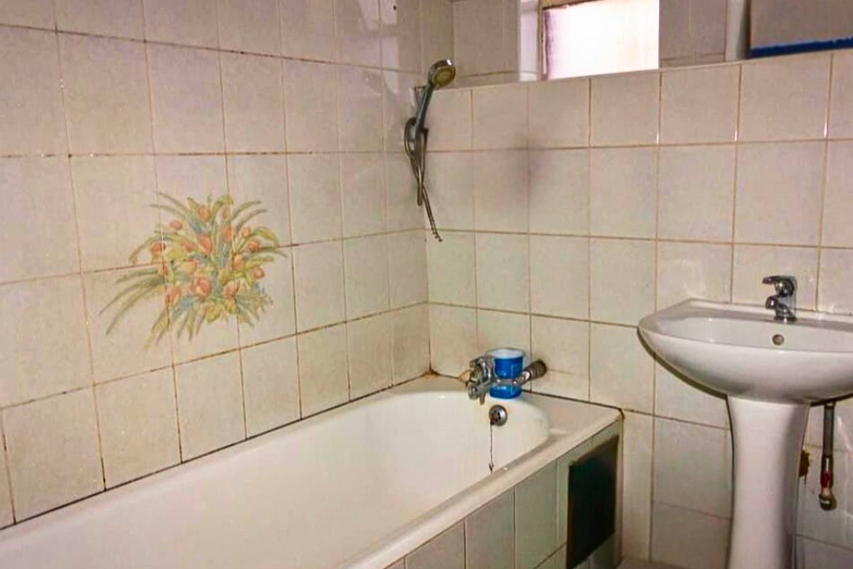 A dated bathroom featuring a pedestal basin and a built-in bathtub with wall-mounted shower fixtures, requiring cosmetic updates to modernize the space.