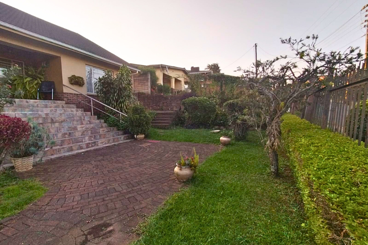 A rear garden area featuring a paved patio, tiered landscaping, stone steps, and established greenery adjacent to the house exterior.