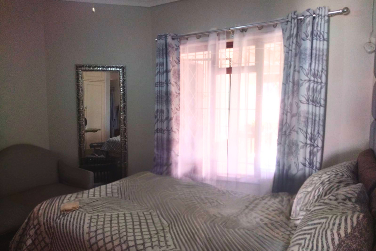 A cozy bedroom featuring a window with security bars, neutral wall finishes, and a ceiling fan.