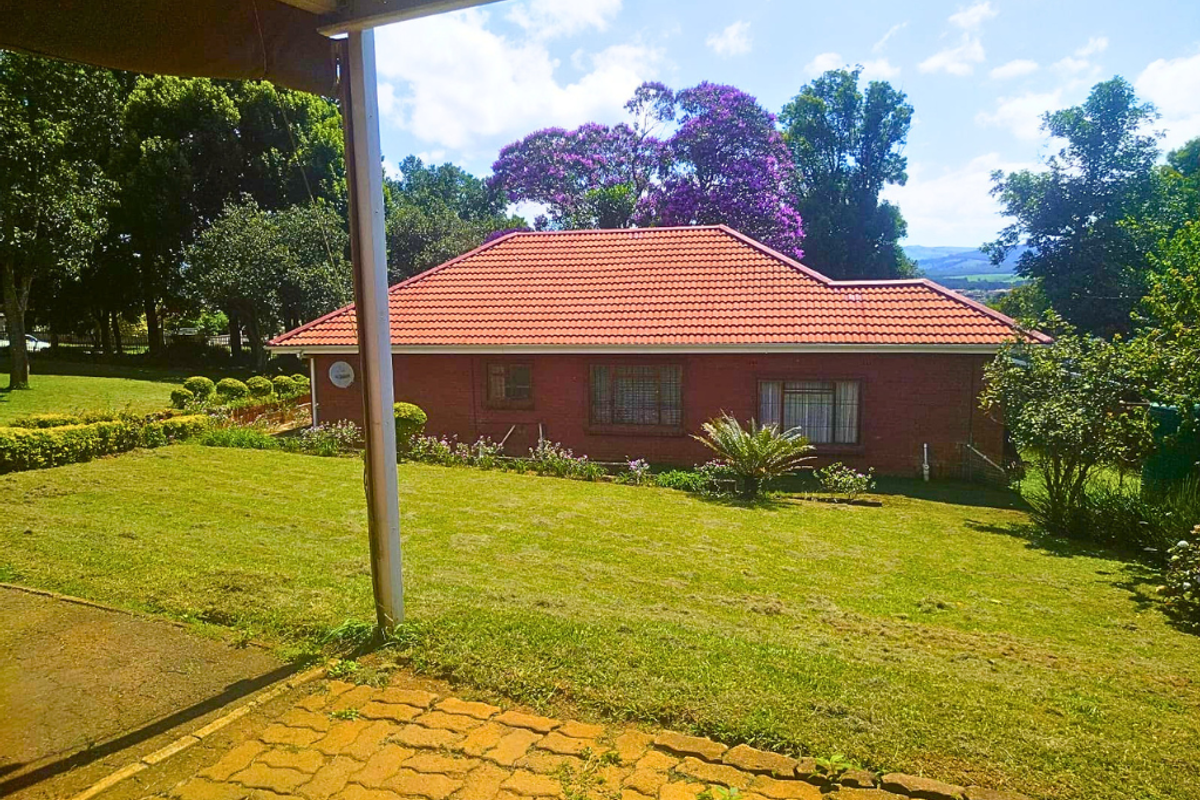 View of the rear brick house exterior featuring a tiled roof, set within a spacious, well-maintained garden with mature trees.