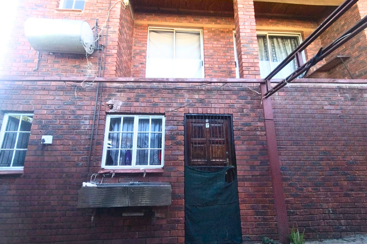 Rear exterior view of a brick house featuring a wall-mounted geyser, security gate, and a utility sink area.