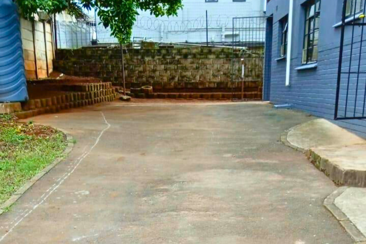 Rear exterior area featuring a concrete paved courtyard, terraced retaining wall, and security fencing adjacent to the apartment building.