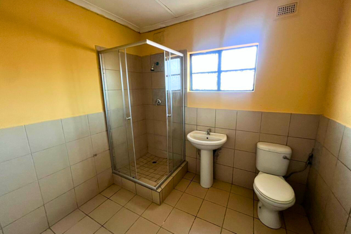 A functional bathroom featuring a corner shower enclosure, pedestal basin, and toilet with tiled flooring and lower wall tiling.