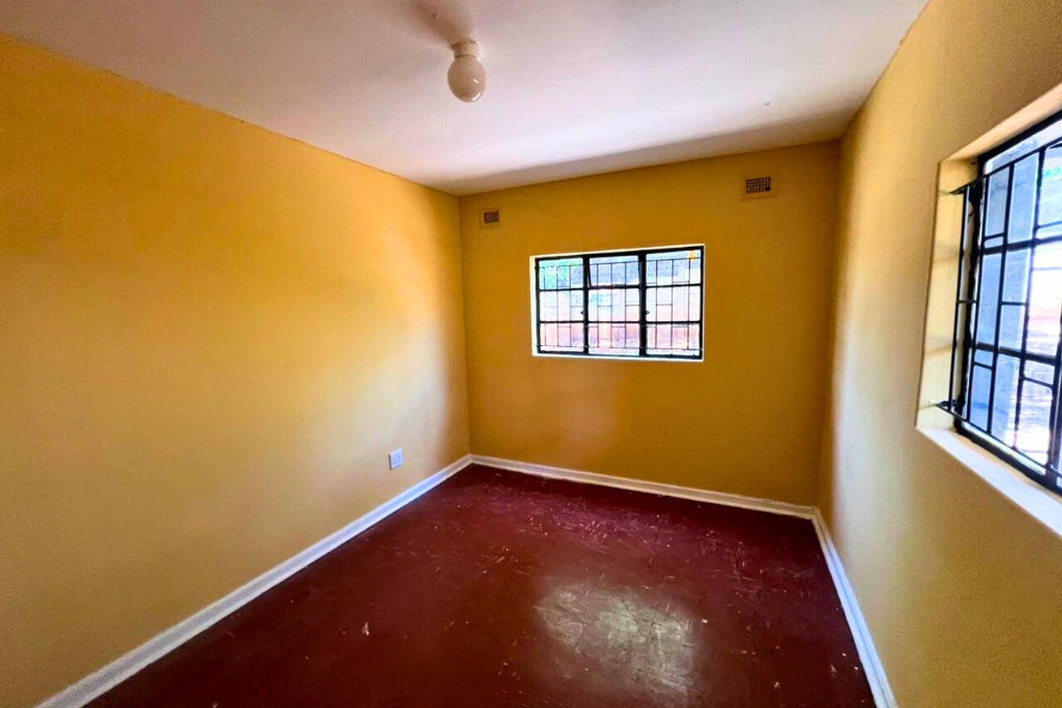 An empty bedroom featuring yellow painted walls, red flooring, and windows fitted with security bars.