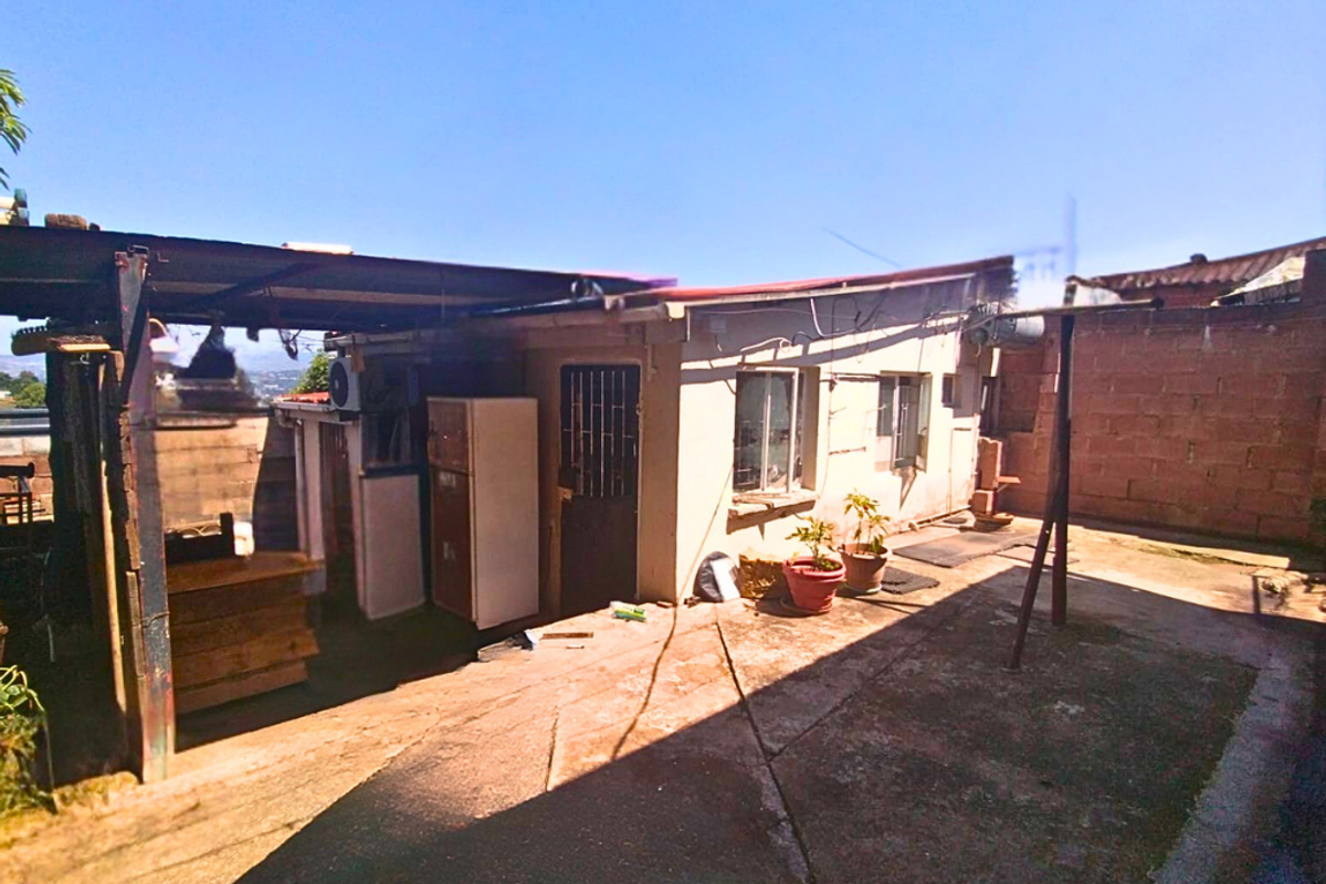 Rear exterior view of the property featuring a concrete courtyard, covered patio area, and basic building facade with security bars on windows.
