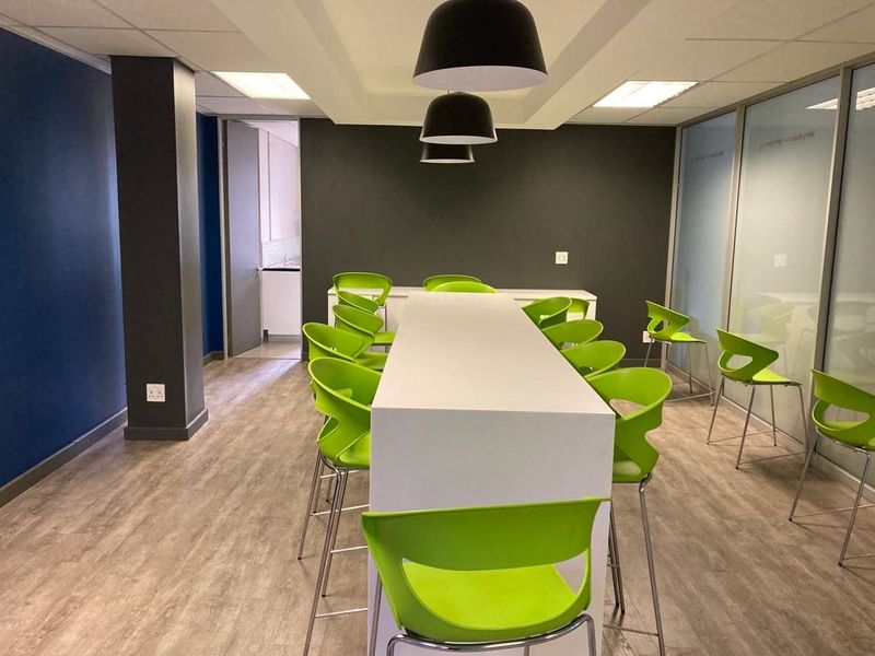 Modern office breakout area featuring laminate flooring, suspended ceiling with recessed lighting, and glass partition walls, creating a bright and professional workspace.