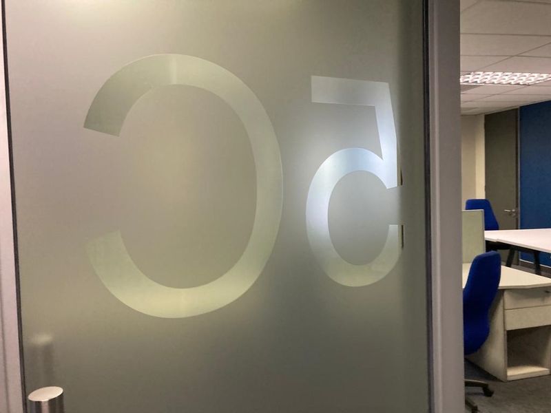 A view through a frosted glass office door into a professional workspace featuring a suspended ceiling and integrated lighting.