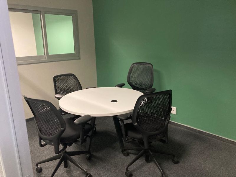 A compact office space featuring a green accent wall, carpeted flooring, and a sliding window for natural light.