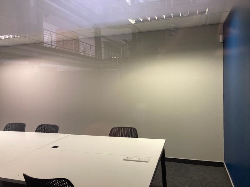 A modern office space featuring a frosted glass partition, recessed ceiling lighting, and carpeted flooring, providing a professional and functional work environment.
