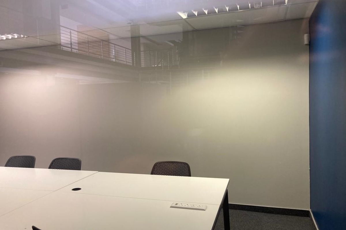 A modern office space featuring a frosted glass partition, recessed ceiling lighting, and carpeted flooring, providing a professional and functional work environment.