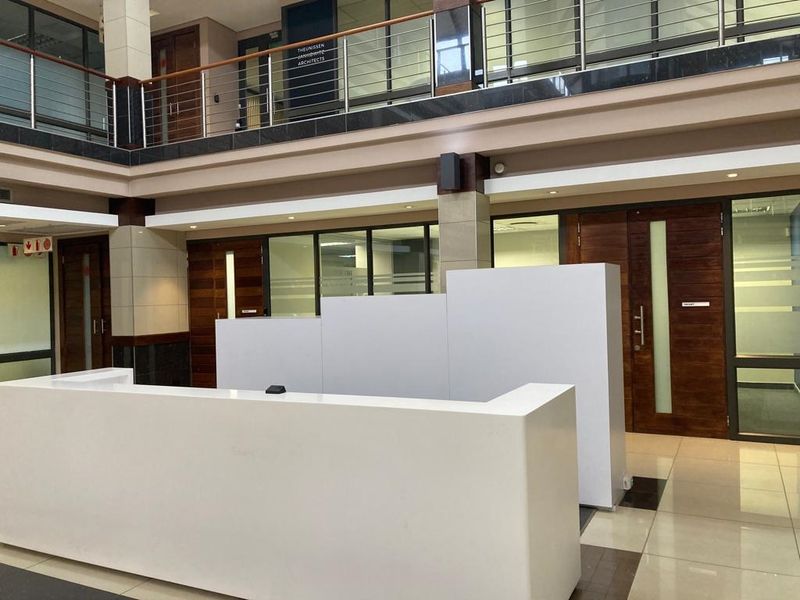 Modern office building entrance lobby featuring a built-in reception desk, tiled flooring, and mezzanine level with glass balustrades.