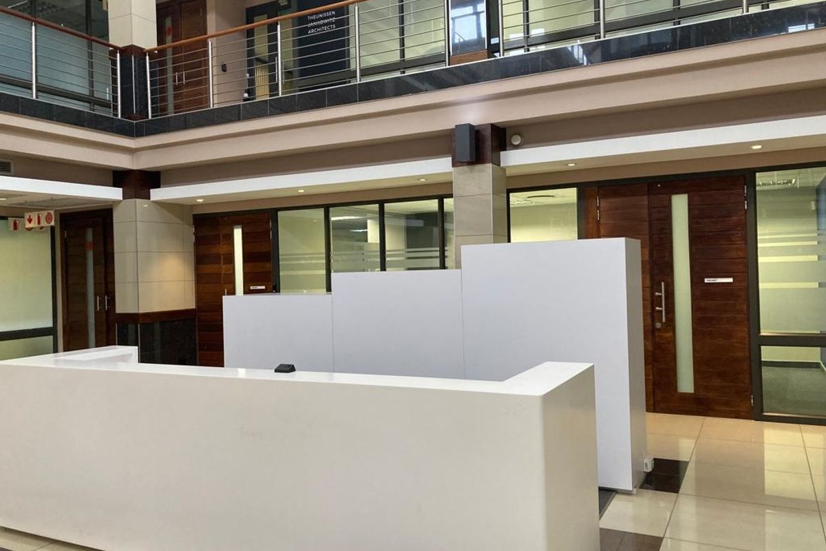 Modern office building entrance lobby featuring a built-in reception desk, tiled flooring, and mezzanine level with glass balustrades.