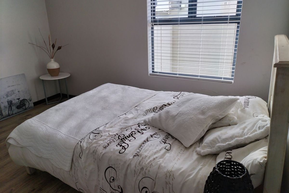 A well-lit bedroom featuring laminate flooring and venetian blinds, providing a neutral and comfortable living space.